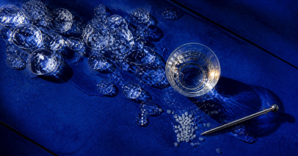 A glass of chilled sake beside melting ice and polished rice on a cobalt-blue surface
