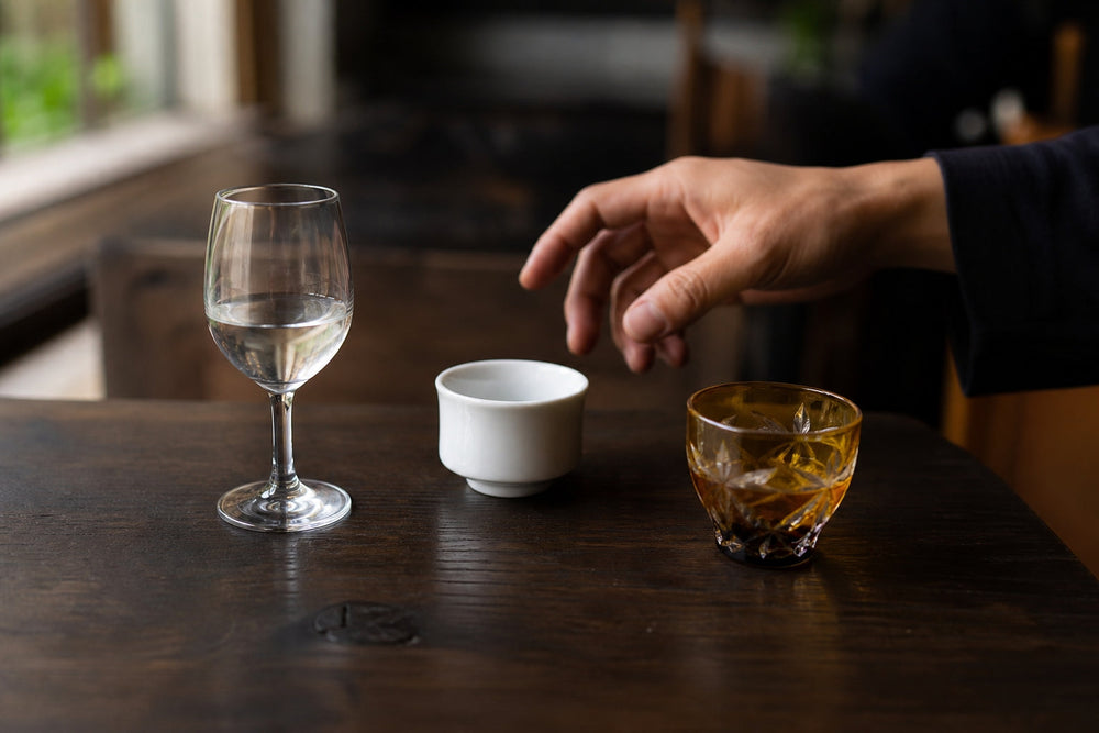 A sake tasting flight served in a wine glass, porcelain cup, and cut-glass cup.