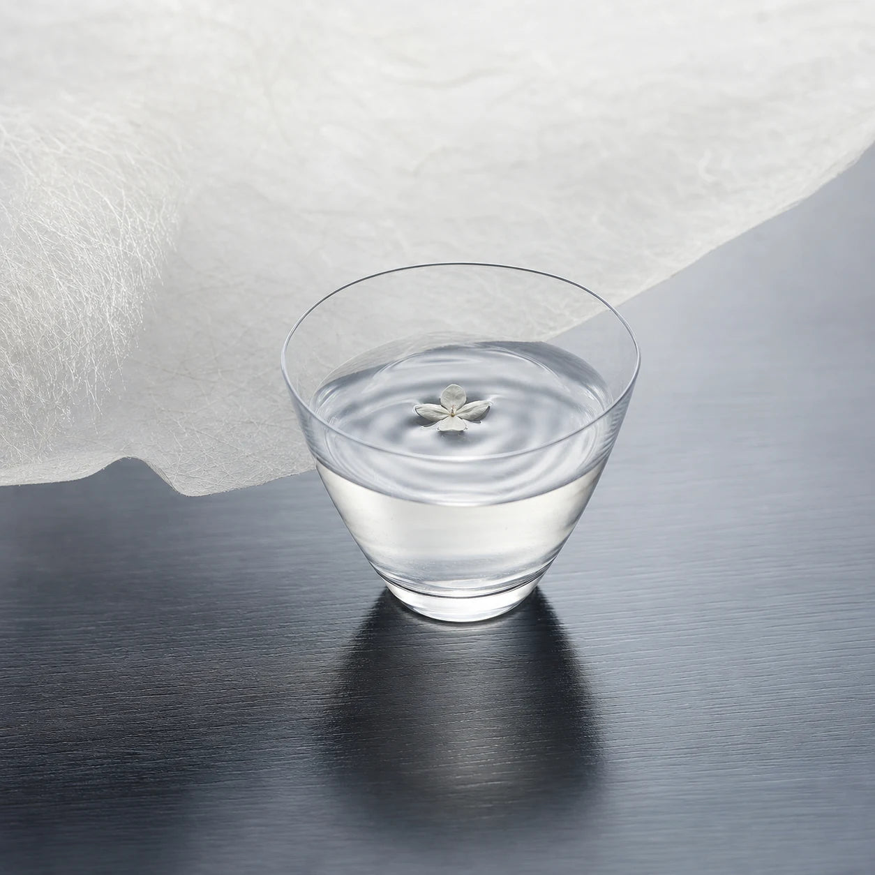 A delicate clear sake glass with a white blossom and soft ripples