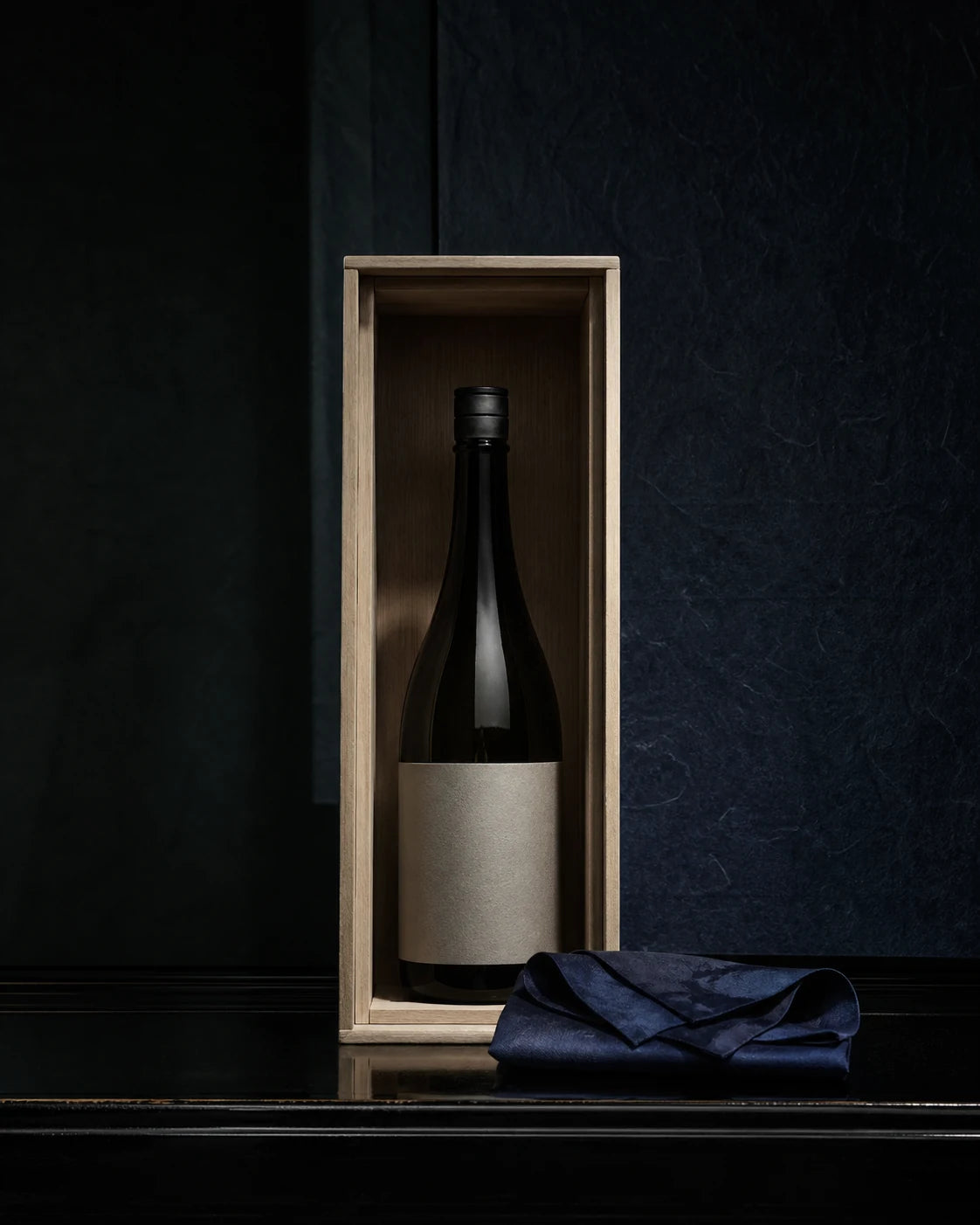 A rare dark sake bottle presented in a paulownia wood display box with indigo cloth